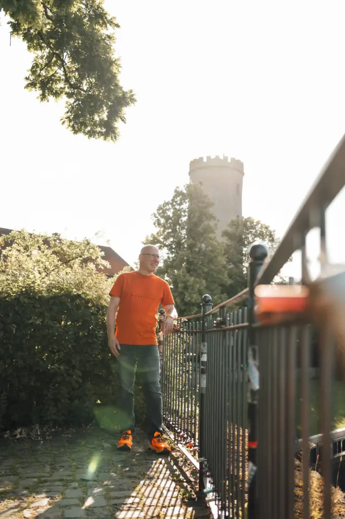 Jörn Kornfeld, Coach für Trennung, steht lächelnd im Freien vor einem historischen Turm.