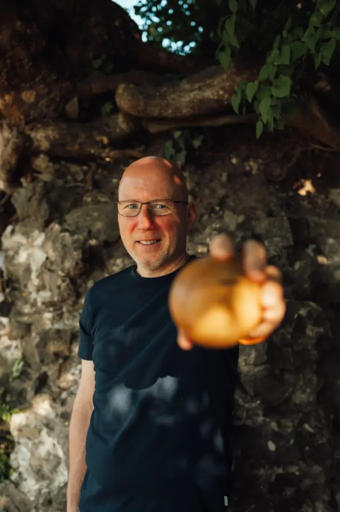 Jörn Kornfeld hält lächelnd einen Apfel in die Kamera und symbolisiert persönliches Wachstum und bewusste Entwicklung.